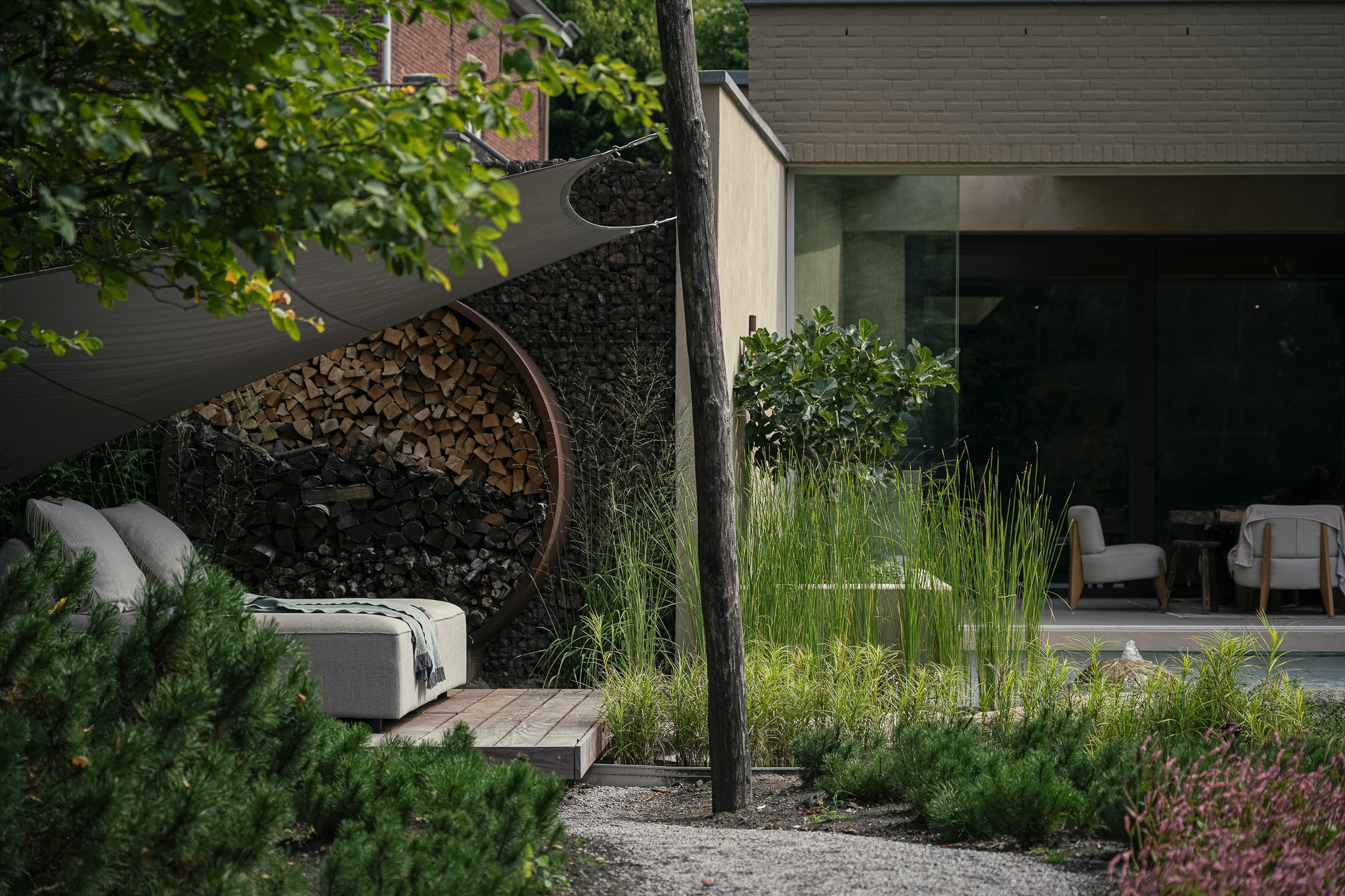 Tuinlounge met circulair houtvak, zeil en riet bij een moderne woning